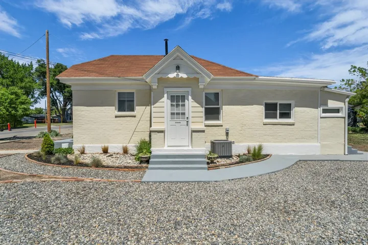Light-colored brick exterior with a peaked roofline, front entry steps, and a gravel driveway