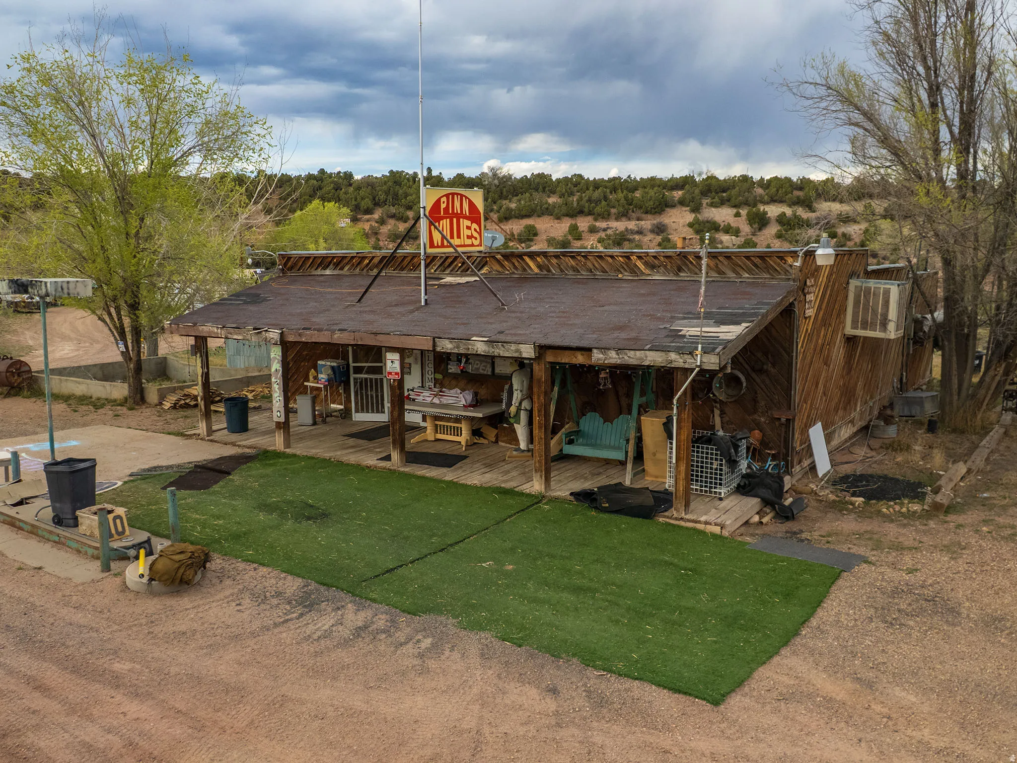 Rustic wood-sided structure with a covered porch featuring exposed wood beams, a flat roof, and an exterior wall-mounted air conditioning unit