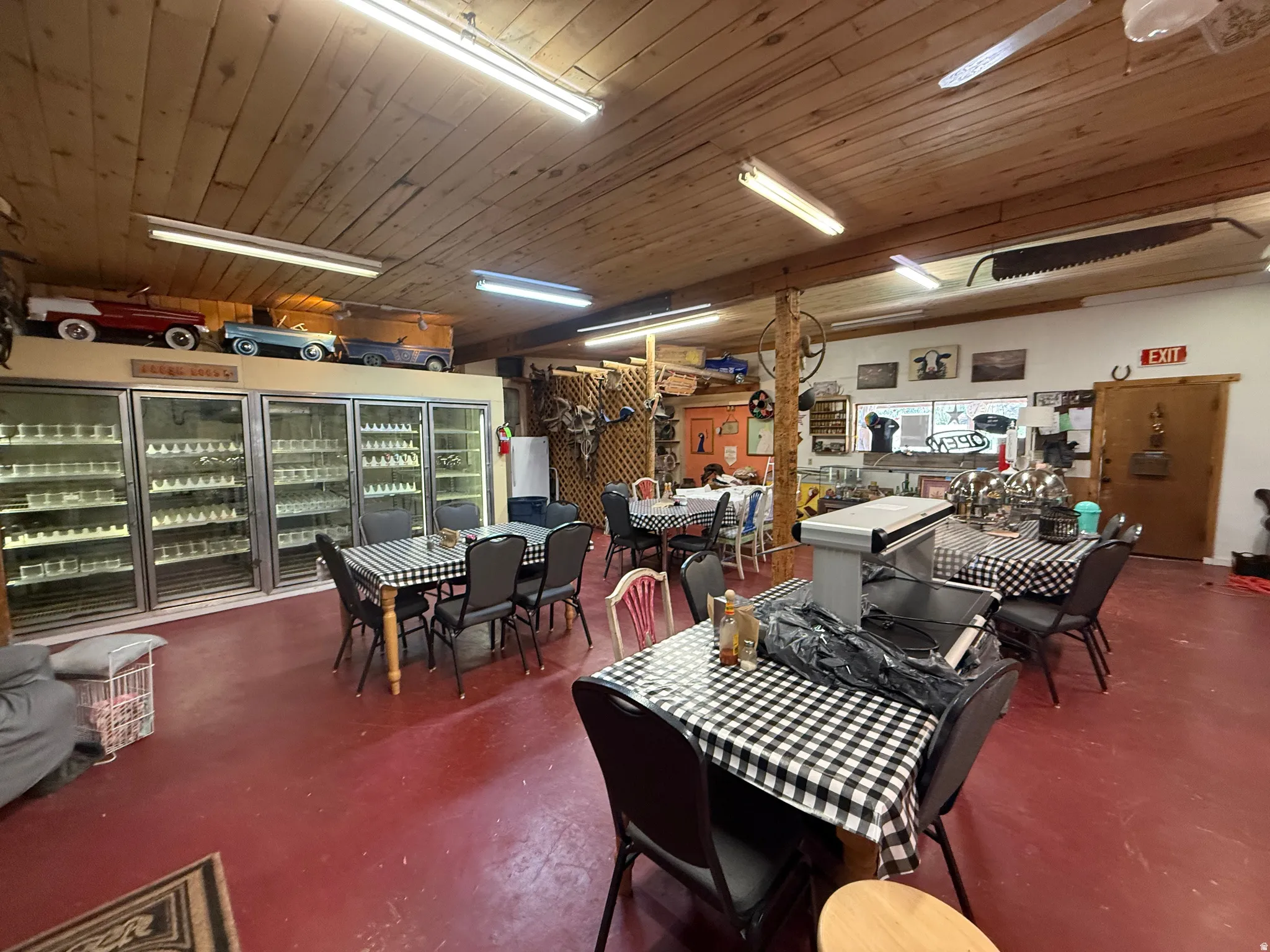 Expansive commercial space featuring a wood-panel ceiling, red flooring, and multiple glass-front refrigeration units