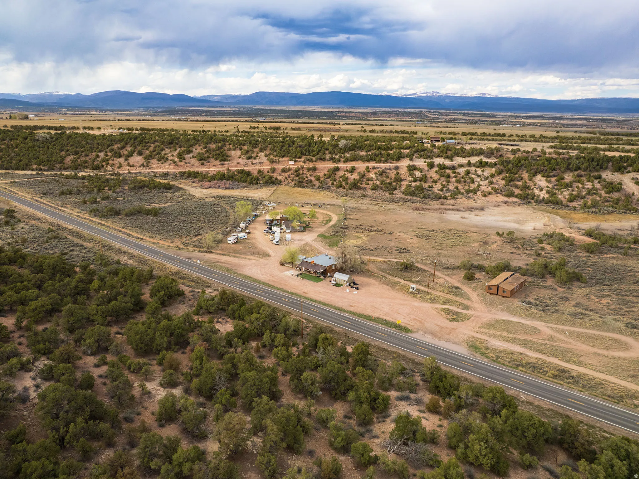 Expansive desert landscape featuring a main residence with outbuildings, a paved roadway, and distant mountains