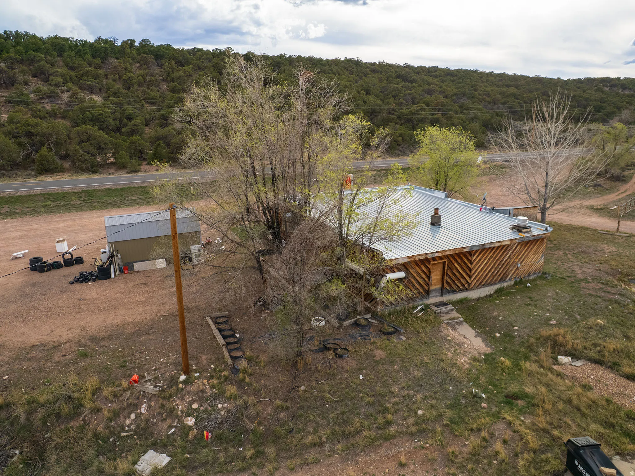 Rustic structure featuring wood panel siding, a corrugated metal roof, a detached utility building with a metal roof, and surrounding natural landscaping