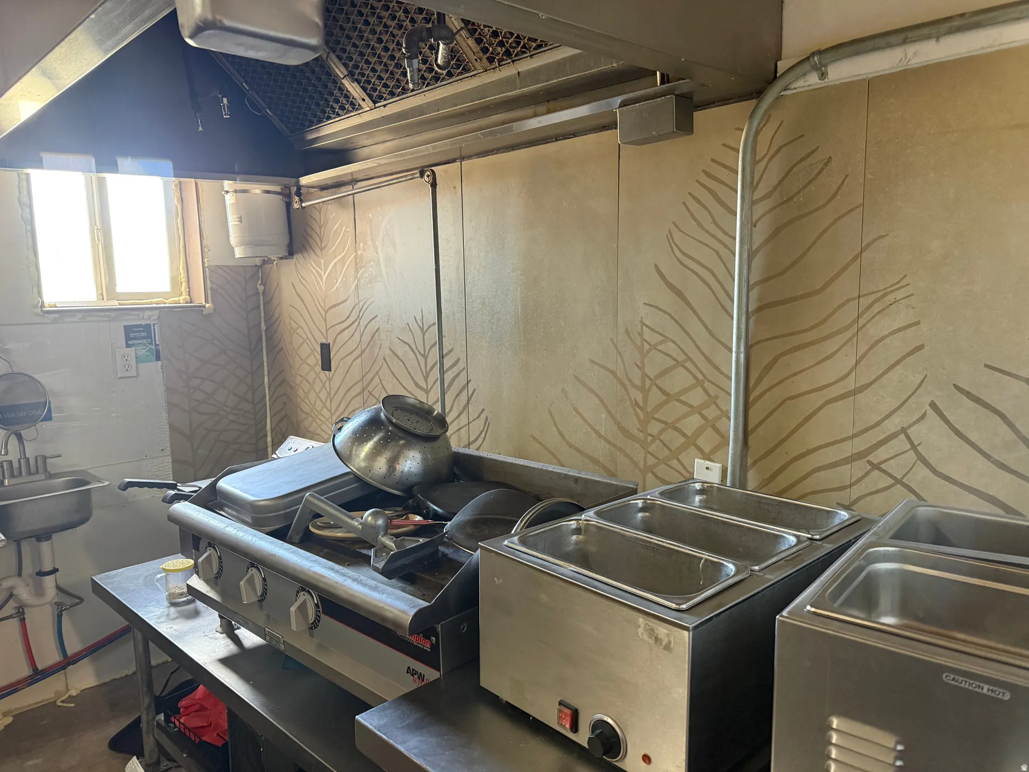 Commercial kitchen space featuring a stainless steel range hood, a four-burner stovetop with a griddle, and multiple countertop warmers
