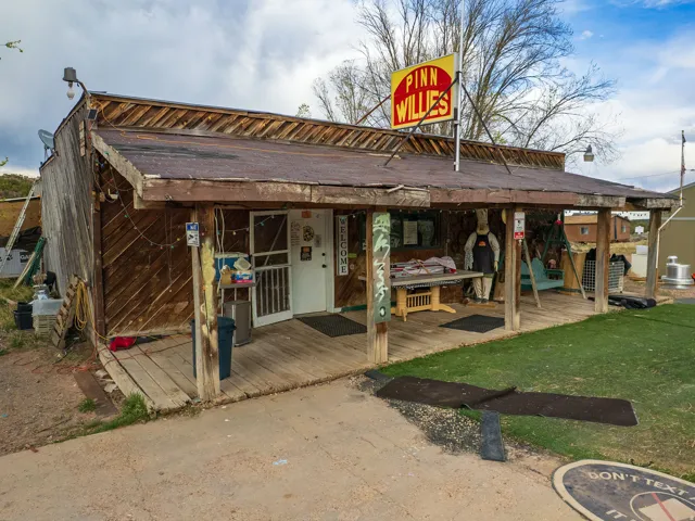 Rustic wood-sided building featuring a covered porch with exposed wood beams, a white entry door, and an overhead sign
