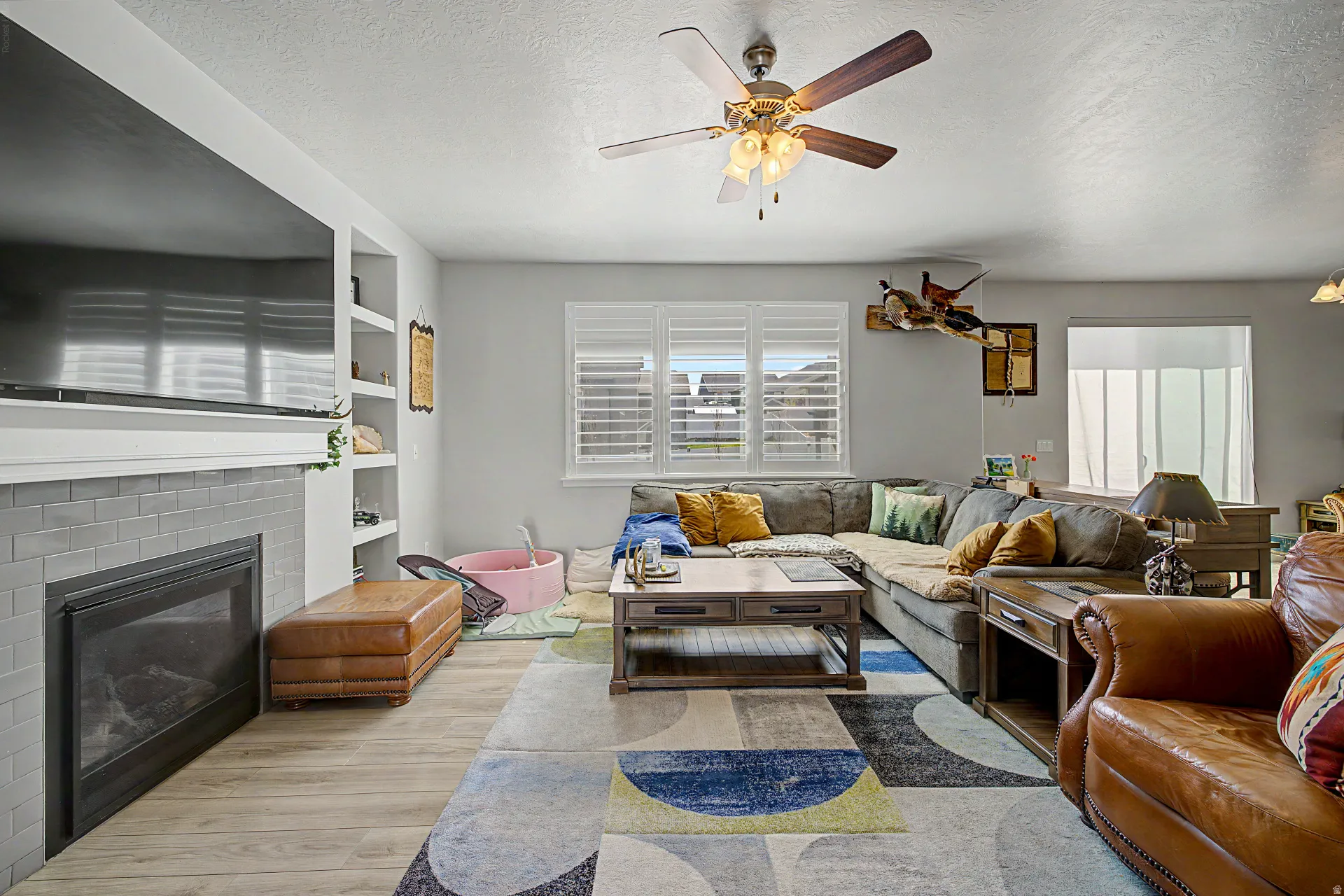 Living room with healthy amount of natural light, a fireplace, a ceiling fan, wood finished floors, and a textured ceiling