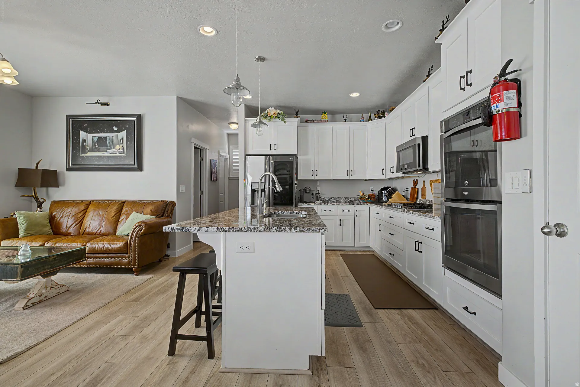 Kitchen with white cabinets, stainless steel appliances, a kitchen bar, decorative light fixtures, and open floor plan