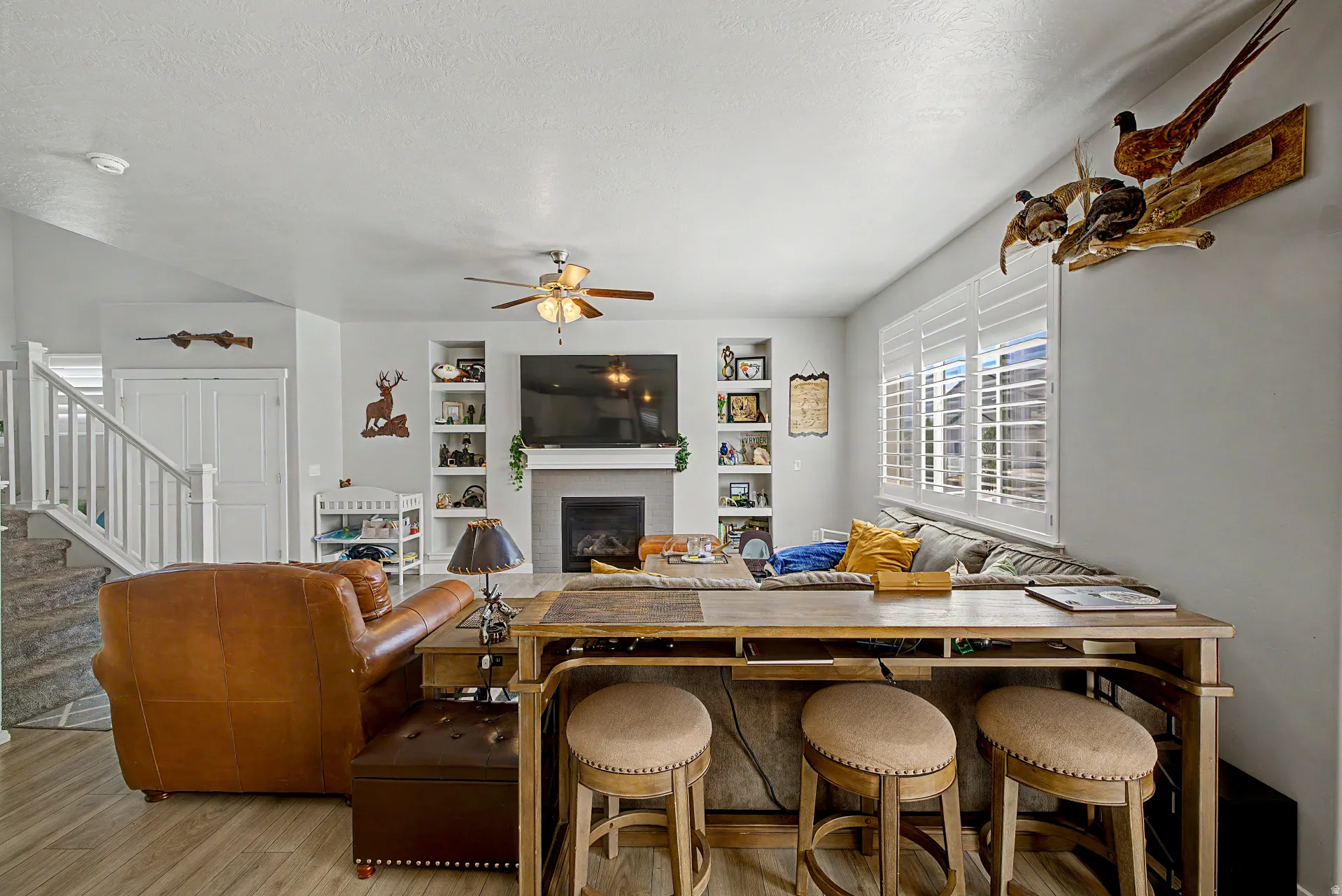 Living room featuring ceiling fan, light wood-style flooring, a fireplace, built in features, and a textured ceiling