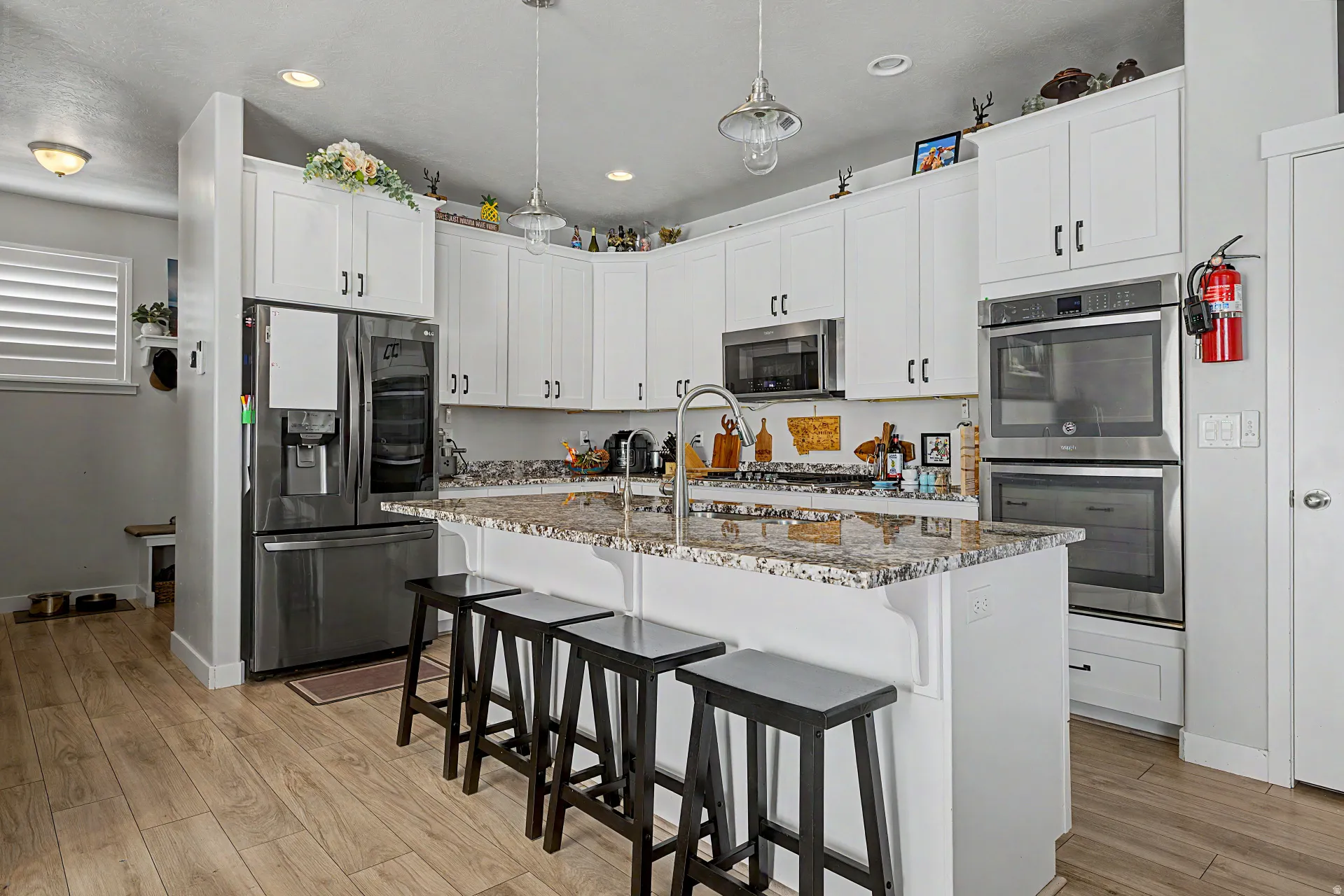 Kitchen featuring a kitchen breakfast bar, white cabinetry, stainless steel appliances, light stone countertops, and a center island with sink
