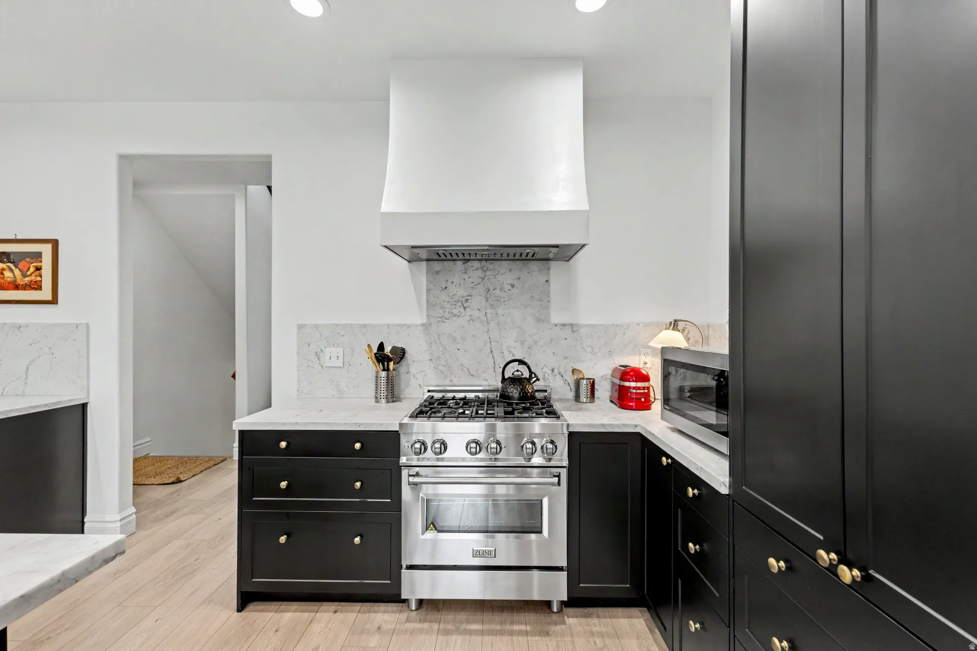 Kitchen featuring dark cabinets, stainless steel appliances, light stone countertops, tasteful backsplash, and light wood-type flooring