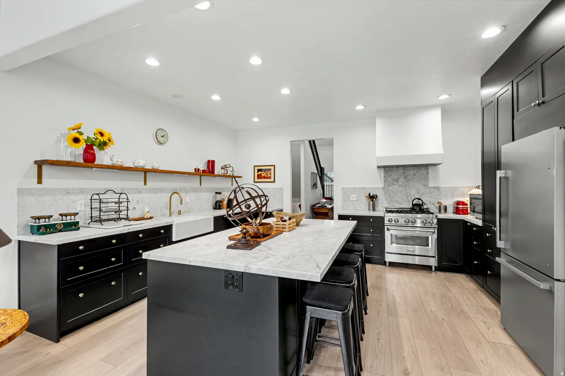Kitchen featuring dark cabinetry, high end appliances, light stone countertops, a breakfast bar, and a kitchen island