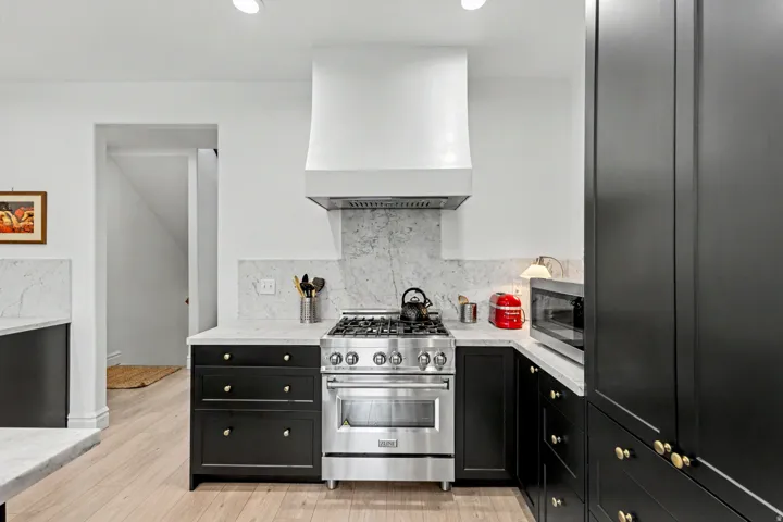 Kitchen featuring dark cabinets, stainless steel appliances, light stone countertops, tasteful backsplash, and light wood-type flooring