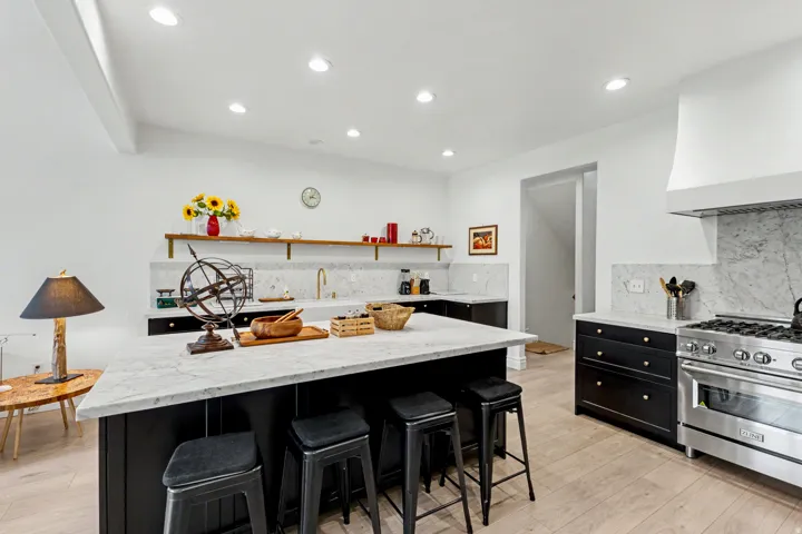 Kitchen with dark cabinetry, light stone counters, high end stove, decorative backsplash, and a breakfast bar