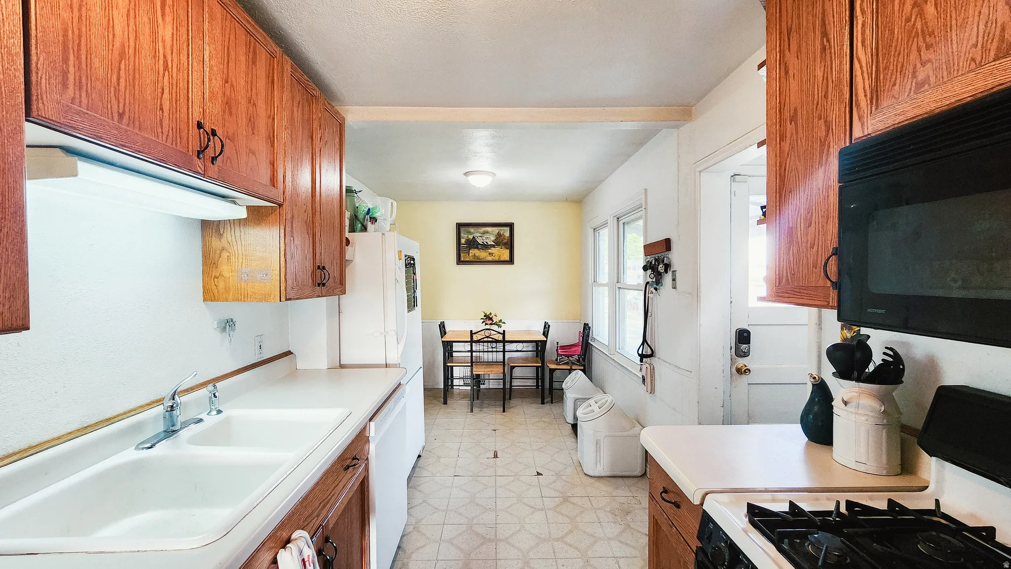 Kitchen with wood finish cabinetry, light floors, range with gas cooktop, black microwave, and light countertops