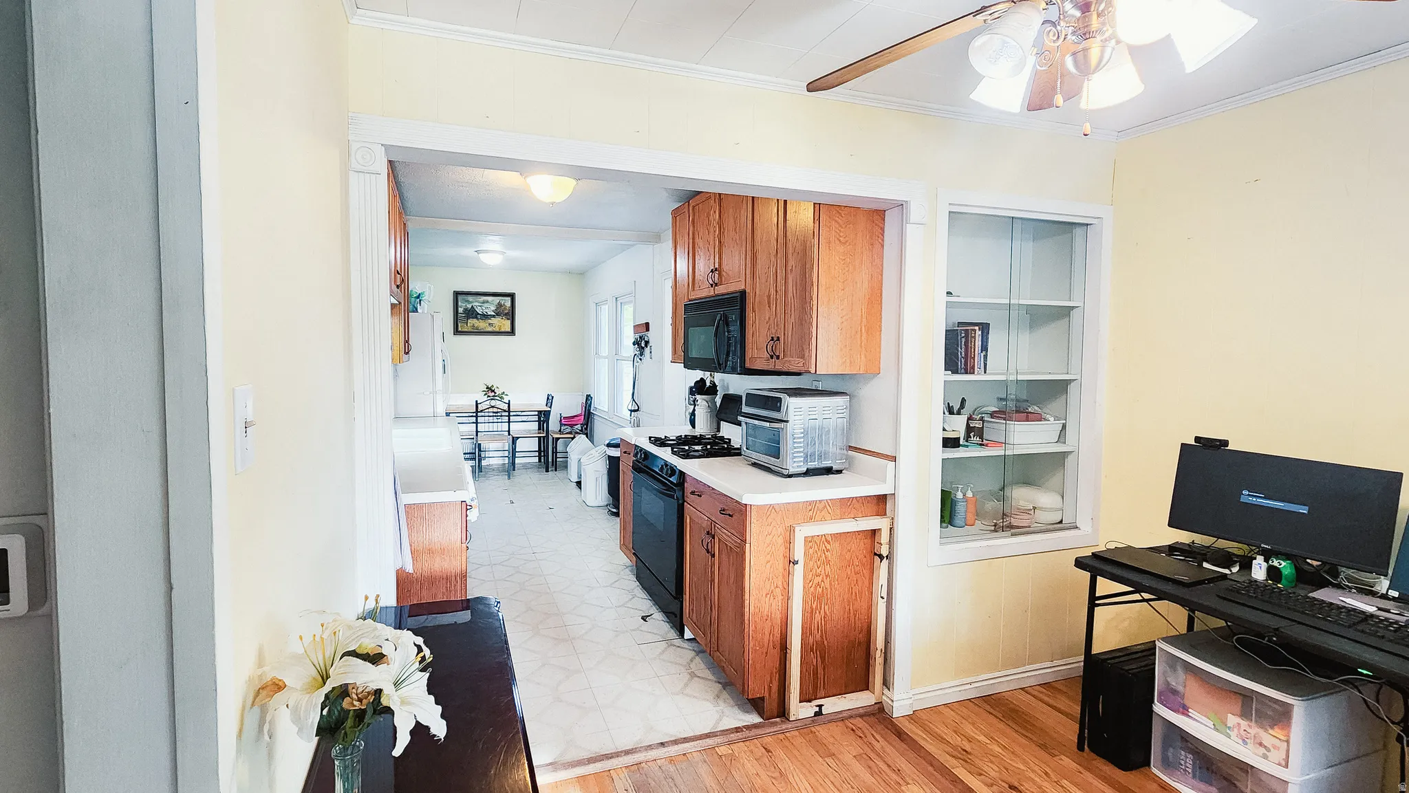 Kitchen with wood finish cabinetry, light countertops, a ceiling fan, black appliances, and light flooring