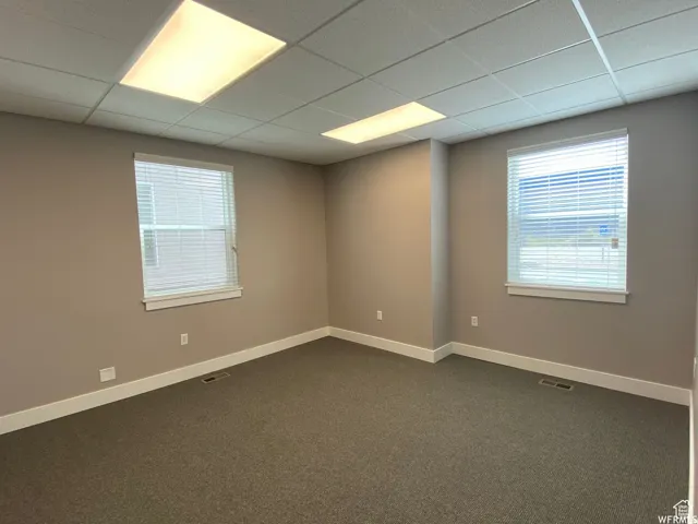Empty room featuring dark carpet and a paneled ceiling