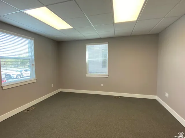 Unfurnished room featuring dark colored carpet, a paneled ceiling, and healthy amount of natural light