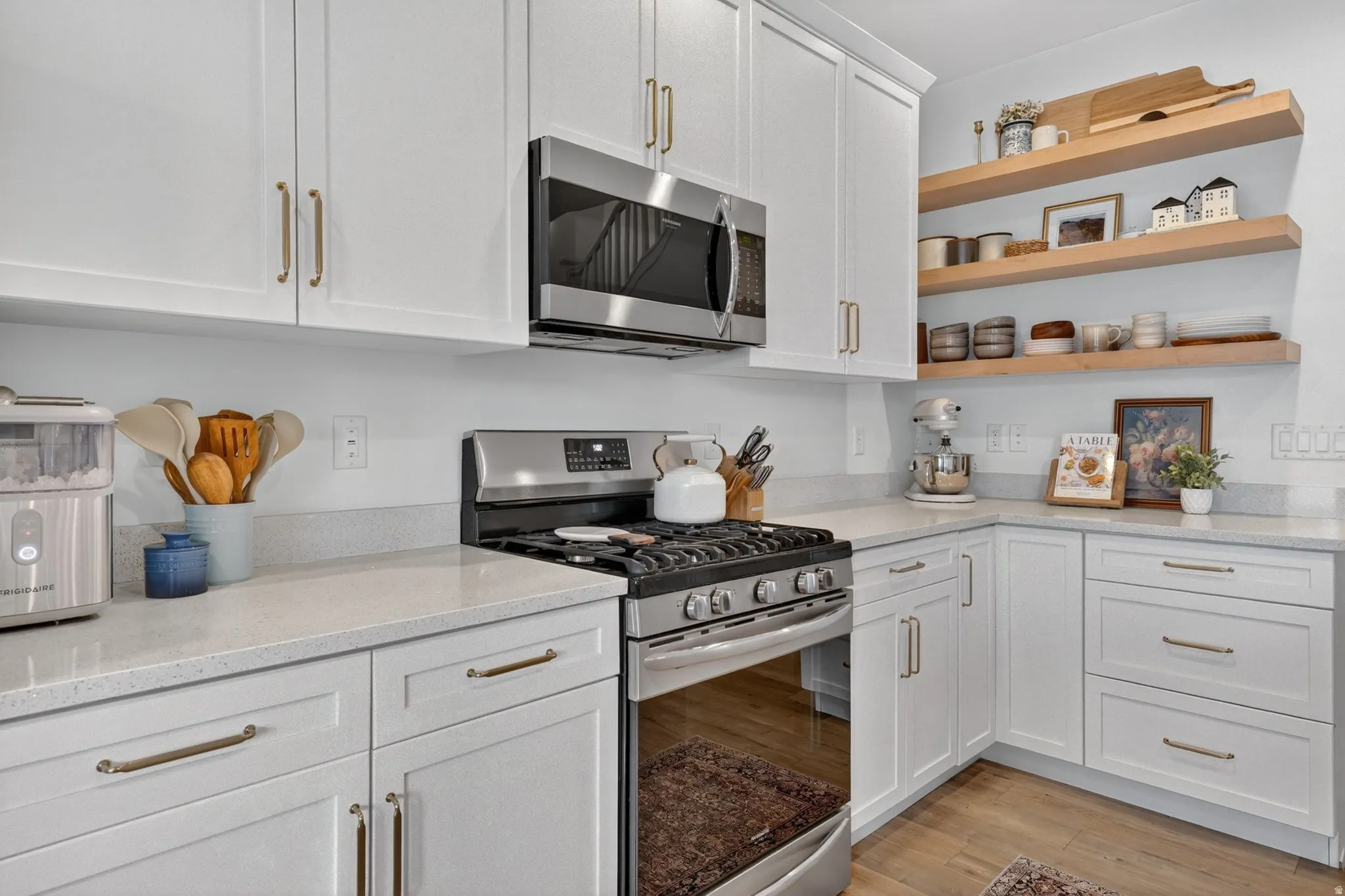 Kitchen featuring stainless steel appliances, white cabinets, light stone countertops, light wood-type flooring, and open shelves