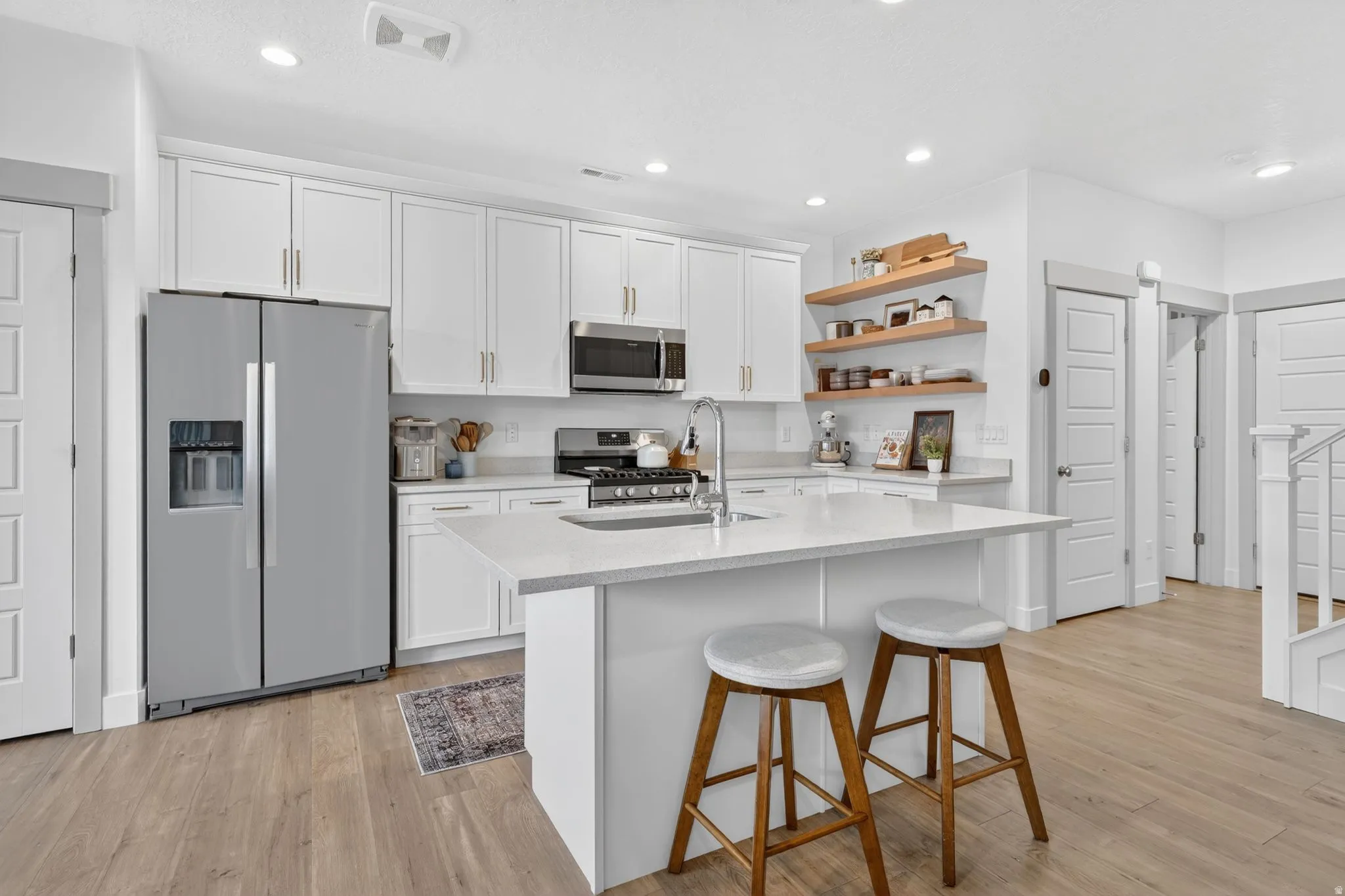 Kitchen featuring stainless steel appliances, white cabinets, a breakfast bar area, light wood-style flooring, and a kitchen island with sink