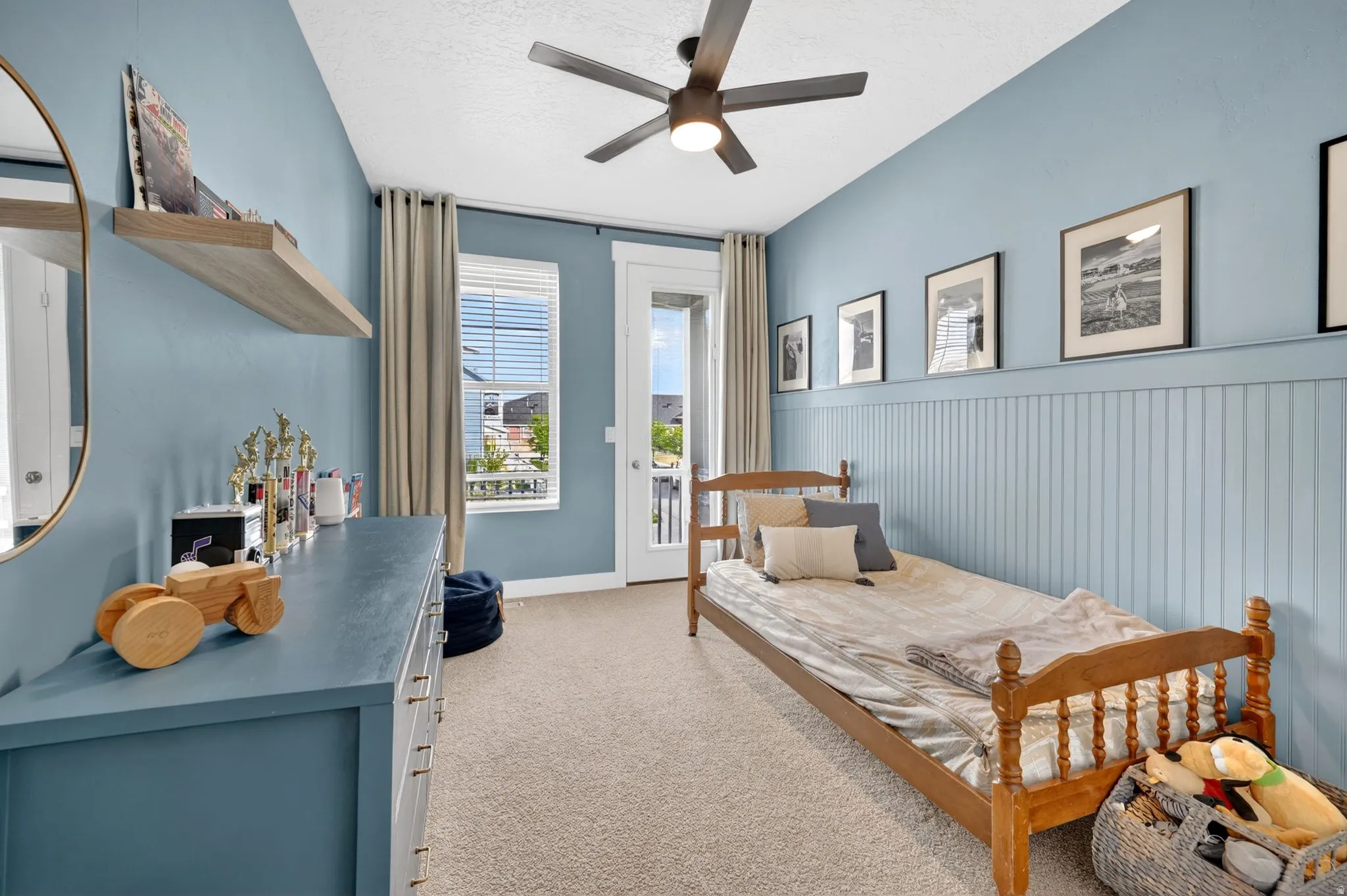 Bedroom with access to outside, wainscoting, a textured ceiling, light colored carpet, and a ceiling fan
