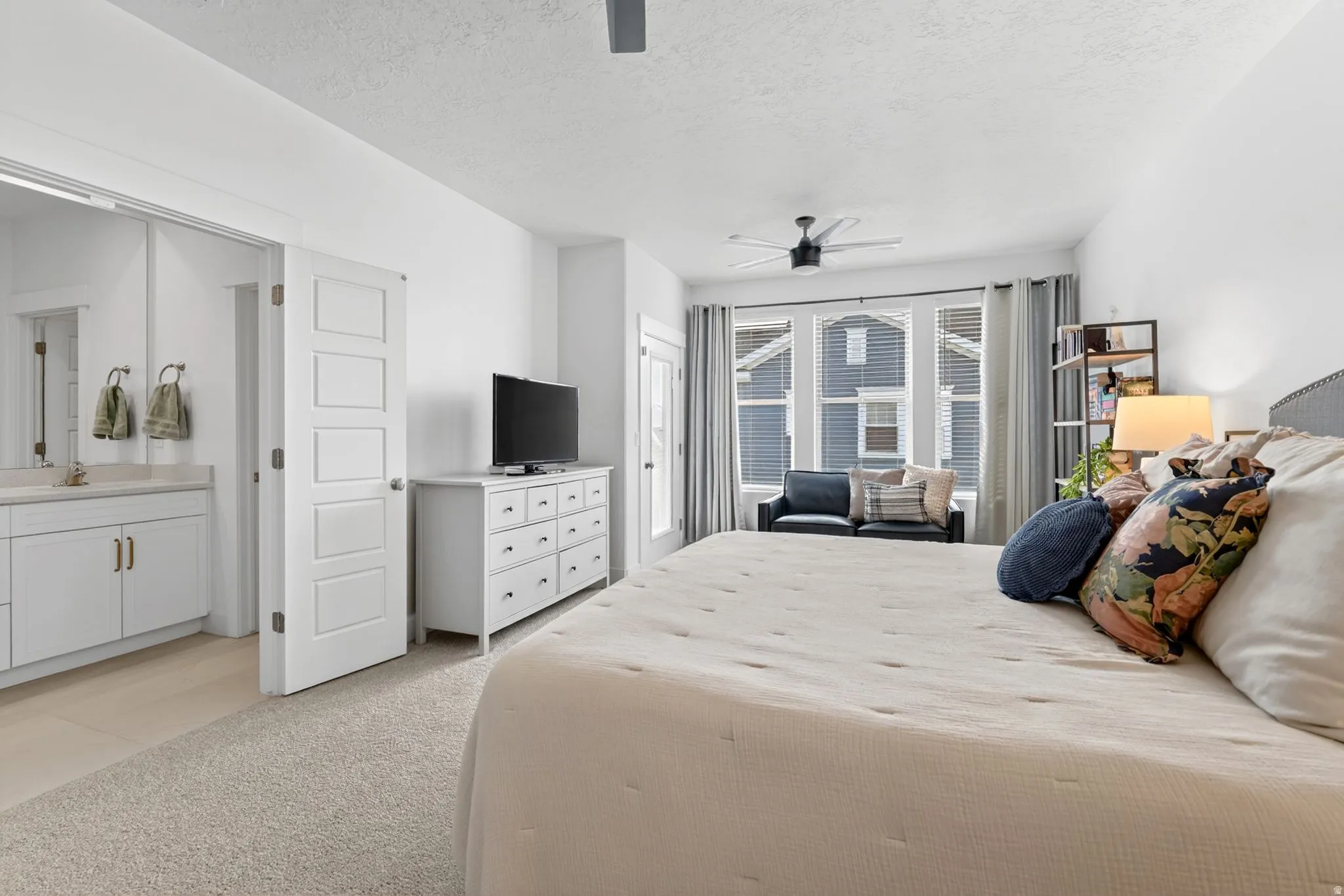 Bedroom with a textured ceiling, light carpet, a ceiling fan, and ensuite bath