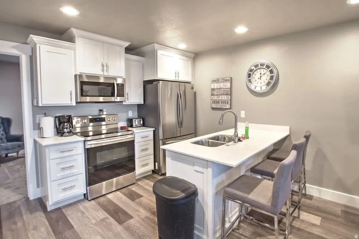 Kitchen featuring stainless steel appliances, a kitchen bar, white cabinetry, dark wood-style flooring, and recessed lighting