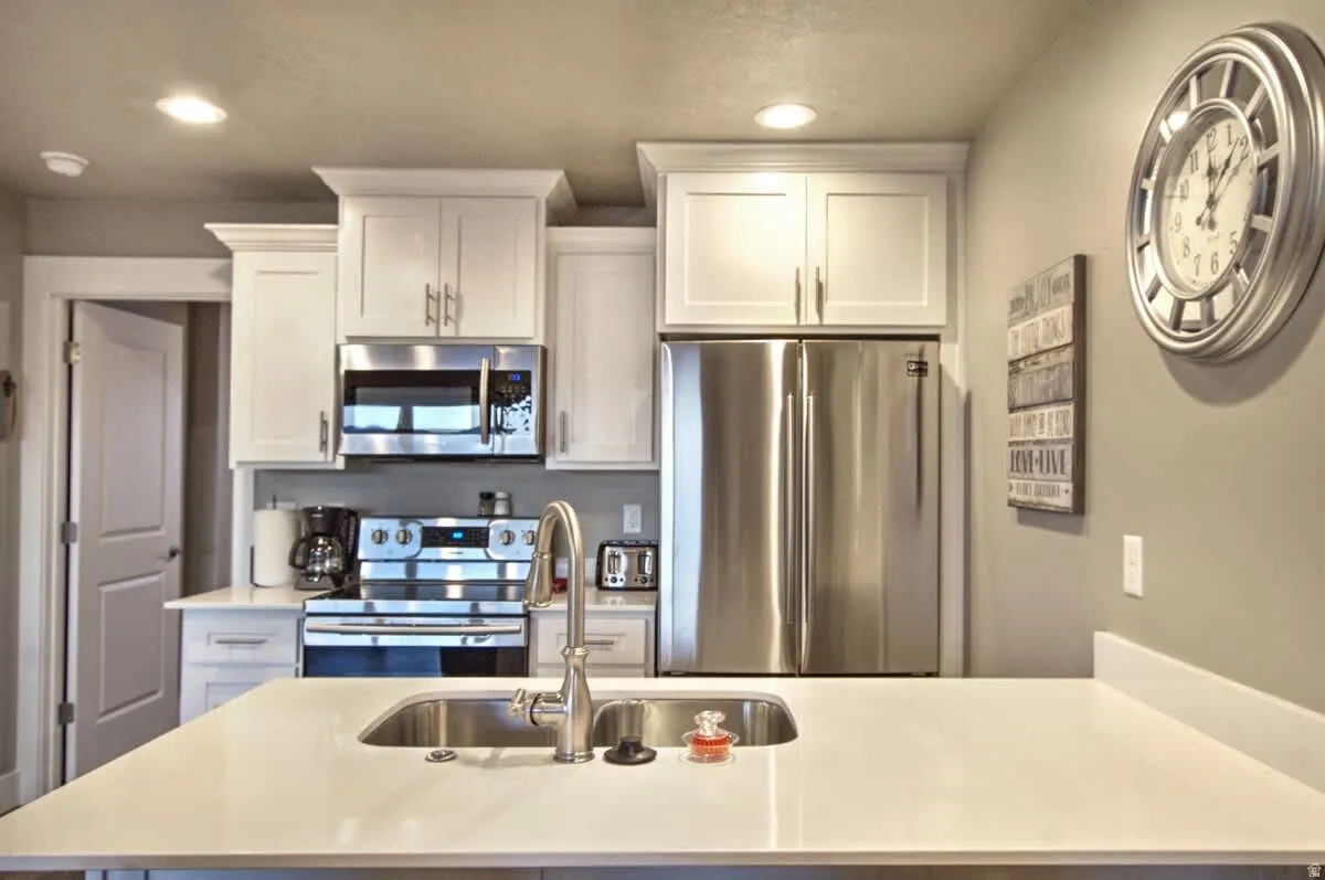 Kitchen featuring stainless steel appliances, white cabinets, recessed lighting, a center island with sink, and light stone counters