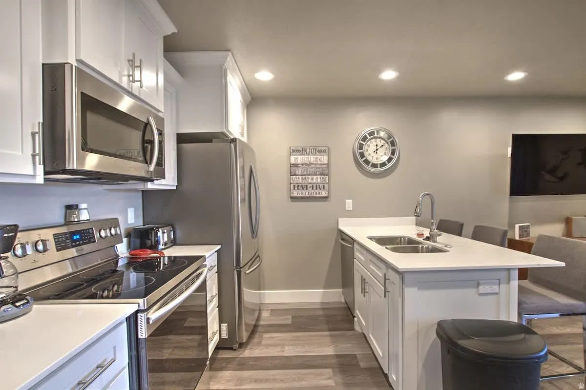 Kitchen with a peninsula, a kitchen bar, stainless steel appliances, white cabinets, and dark wood-type flooring