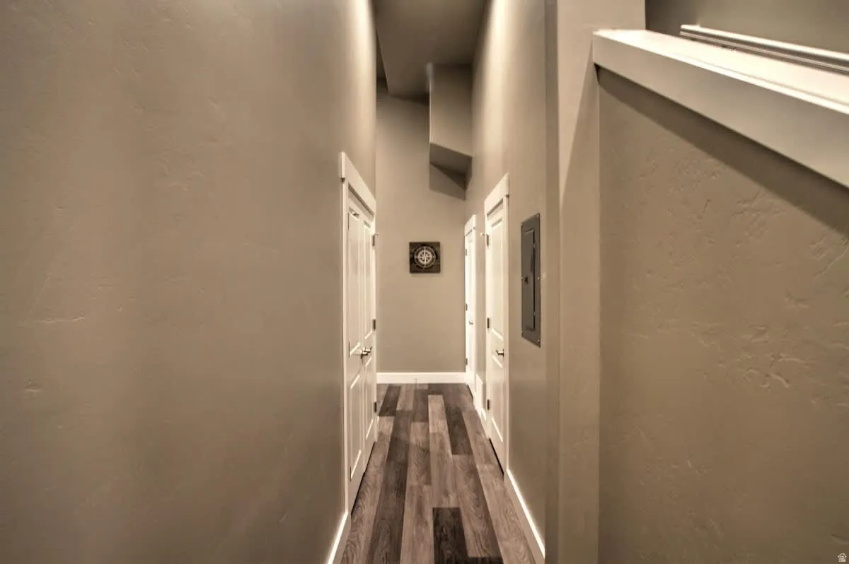 Corridor with a high ceiling, a textured wall, dark wood finished floors, and electric panel