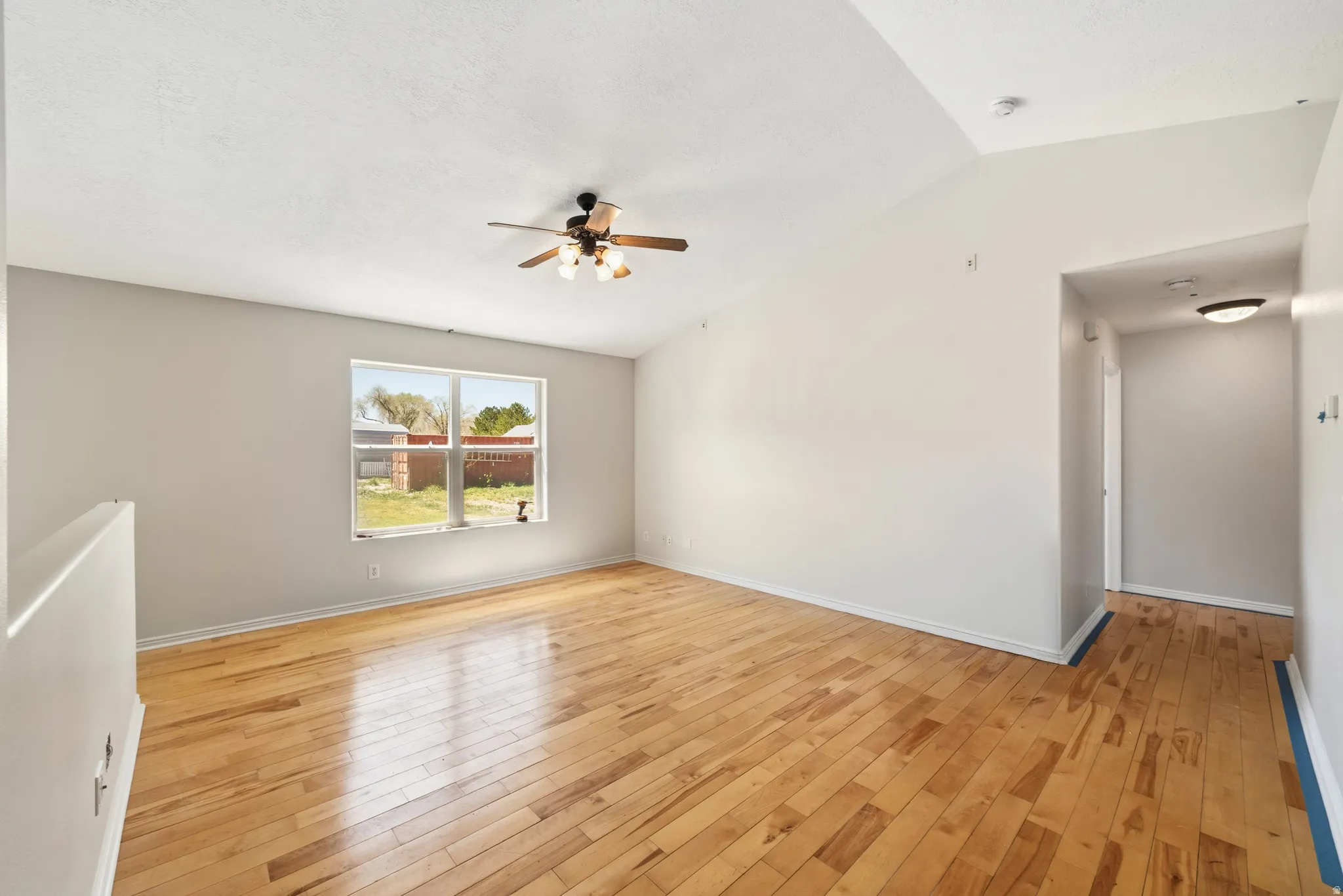 Unfurnished room with light wood-style flooring, lofted ceiling, and a ceiling fan