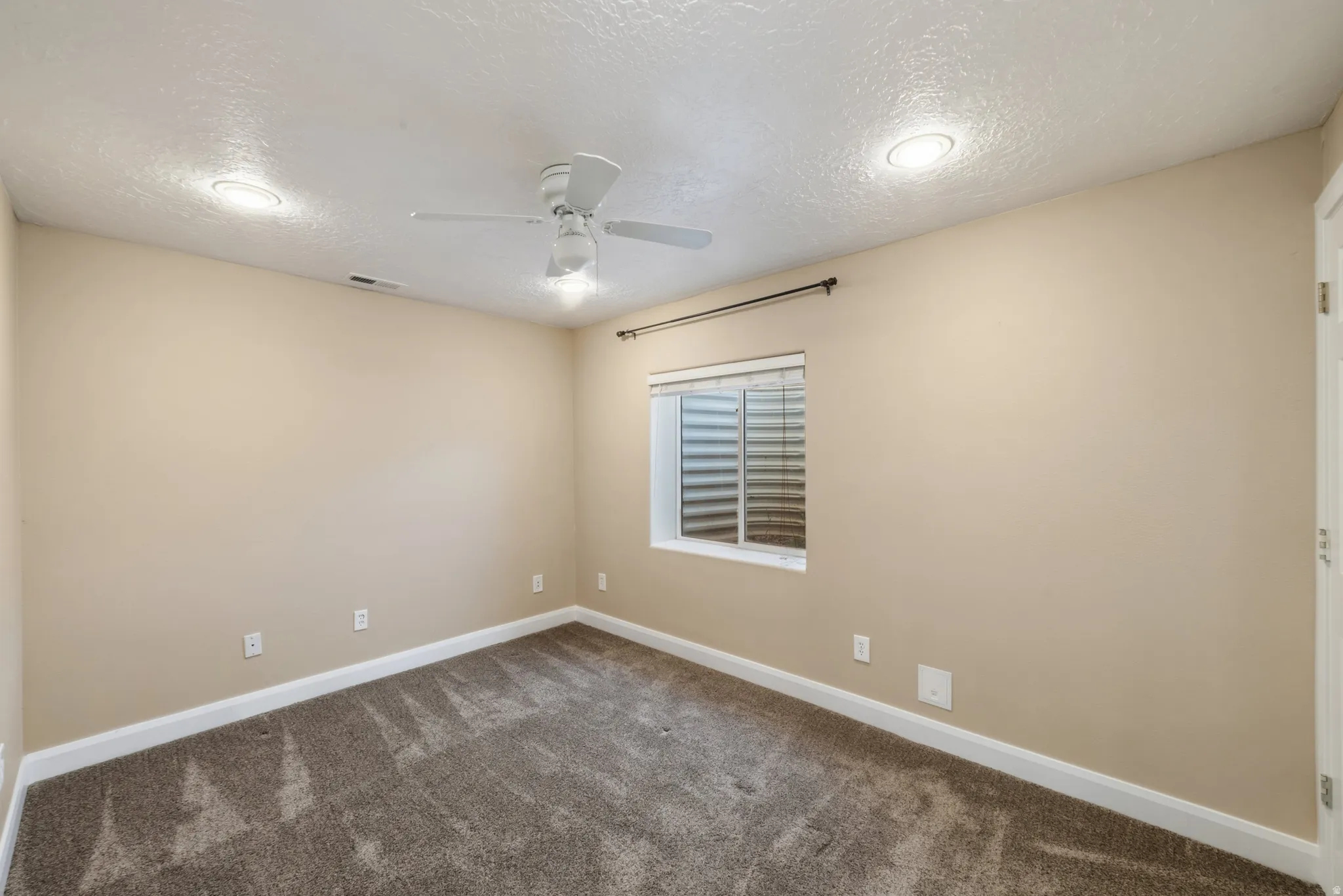 Spare room with a textured ceiling, dark colored carpet, and ceiling fan