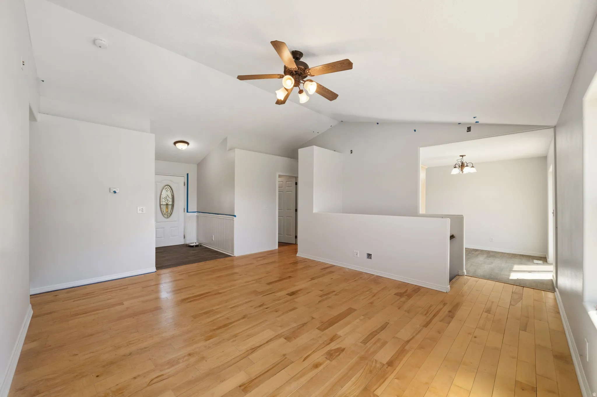 Empty room featuring light wood-style floors, ceiling fan, lofted ceiling, and suspended lighting