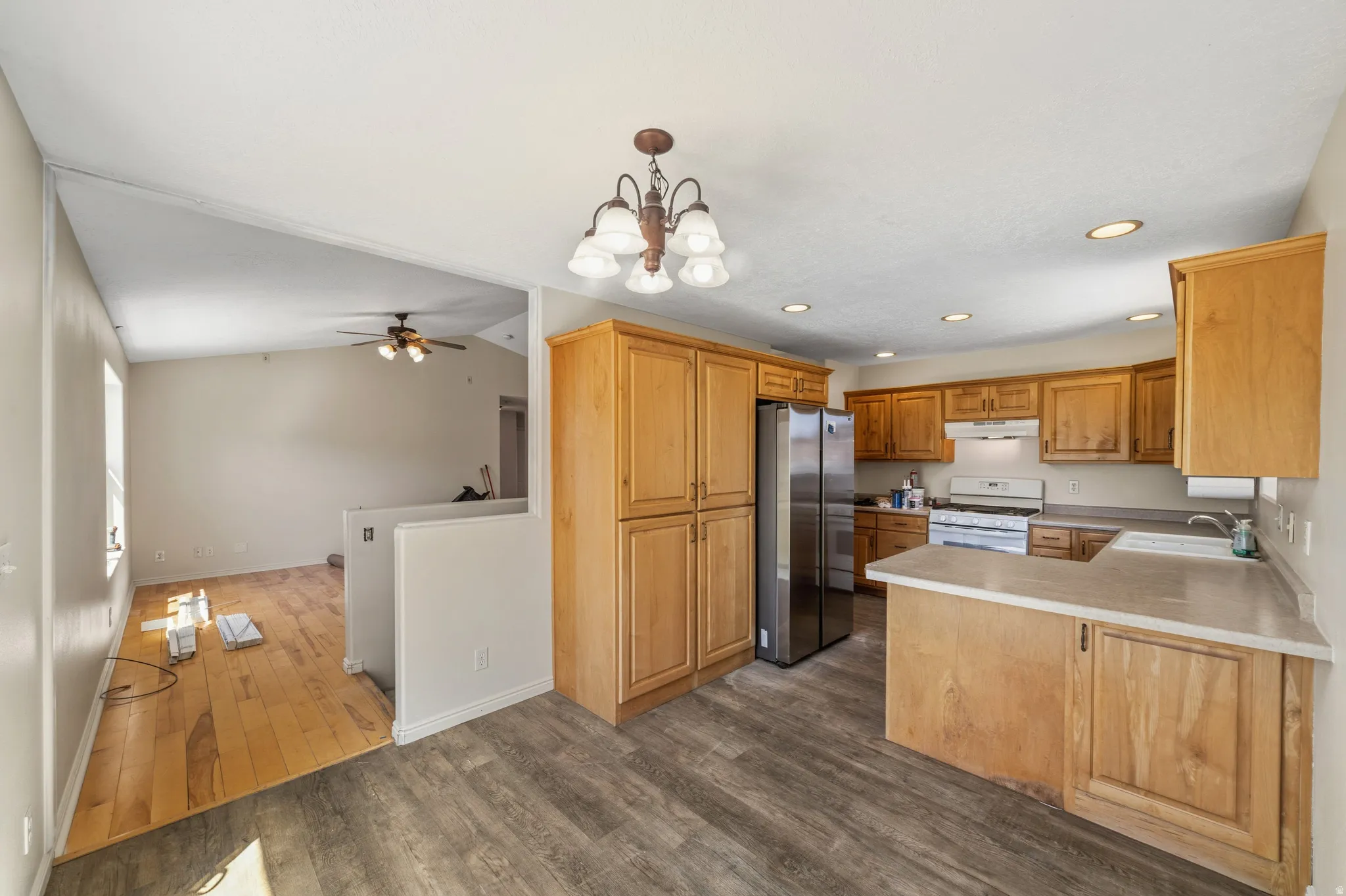 Kitchen featuring a peninsula, a chandelier, freestanding refrigerator, dark wood-type flooring, and light countertops