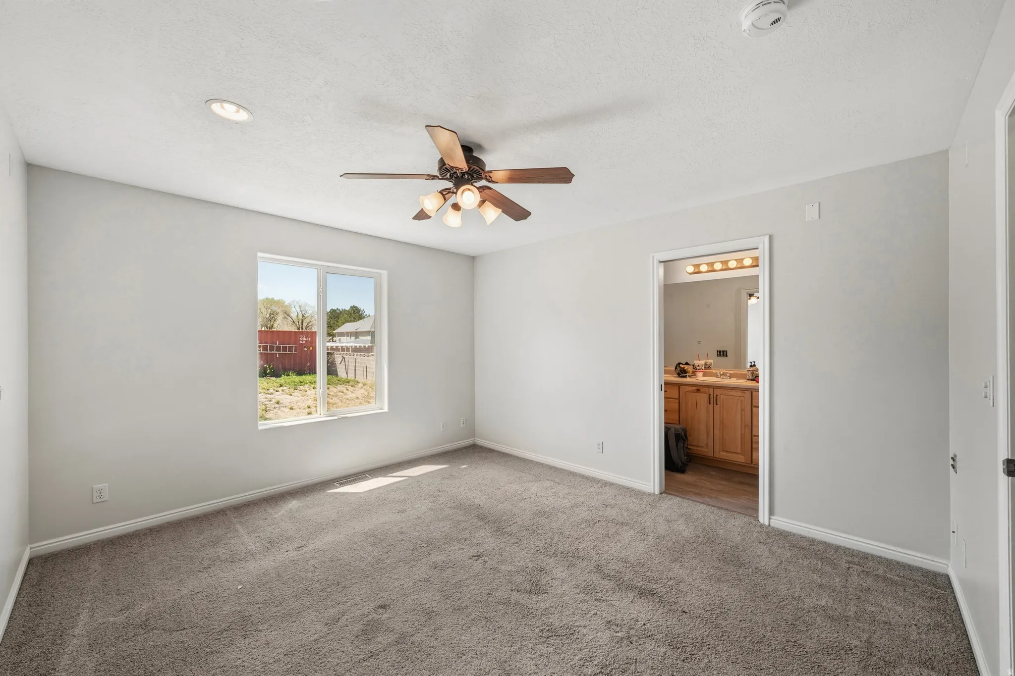 Unfurnished bedroom with carpet, ceiling fan, connected bathroom, and a textured ceiling