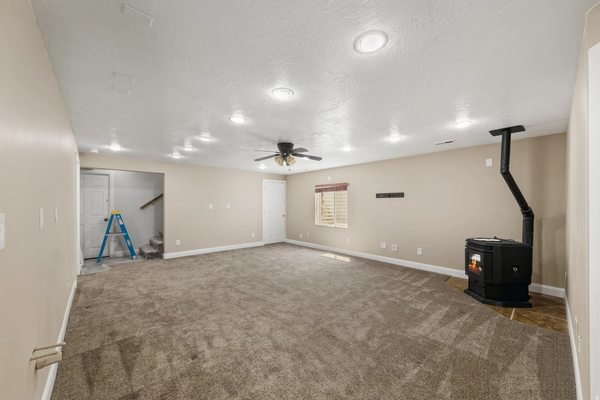 Basement featuring a wood stove, a ceiling fan, a textured ceiling, and carpet floors
