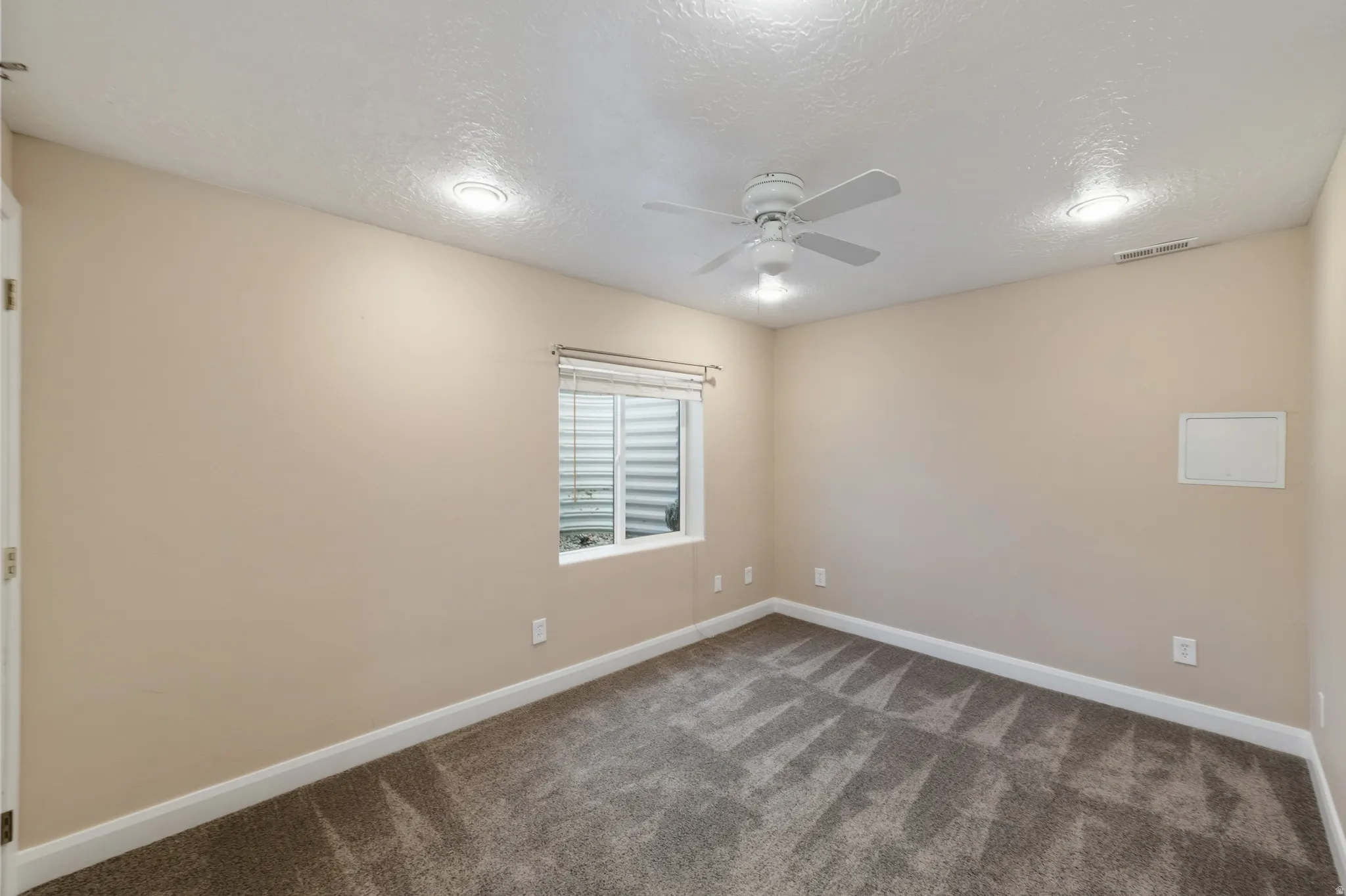 Unfurnished room with a textured ceiling, a ceiling fan, and dark carpet