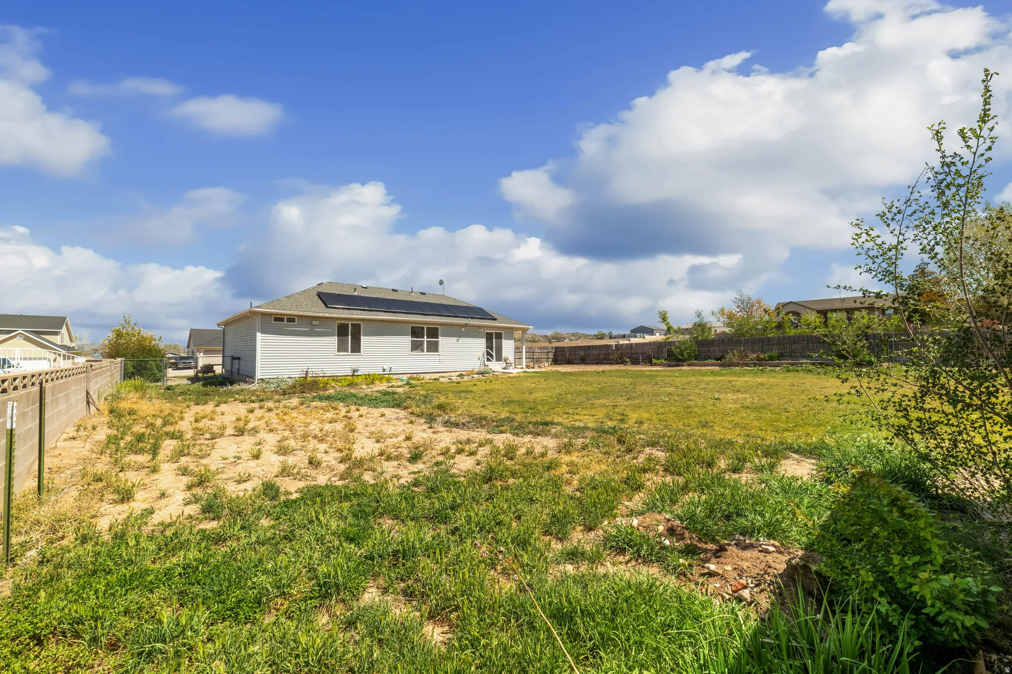 Back of house with solar panels and a fenced backyard