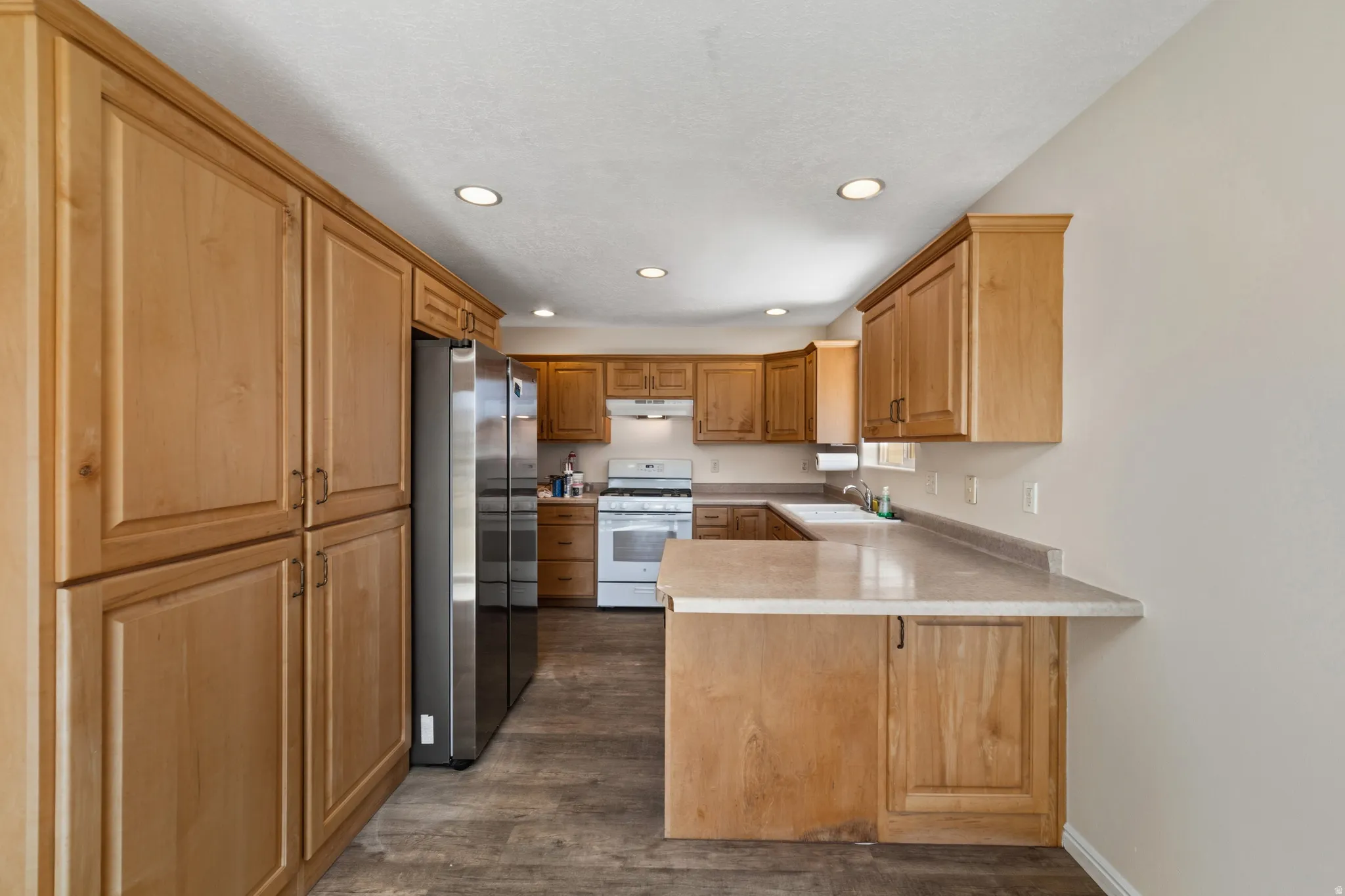 Kitchen featuring a peninsula, freestanding refrigerator, white range with gas stovetop, light countertops, and dark wood-style floors