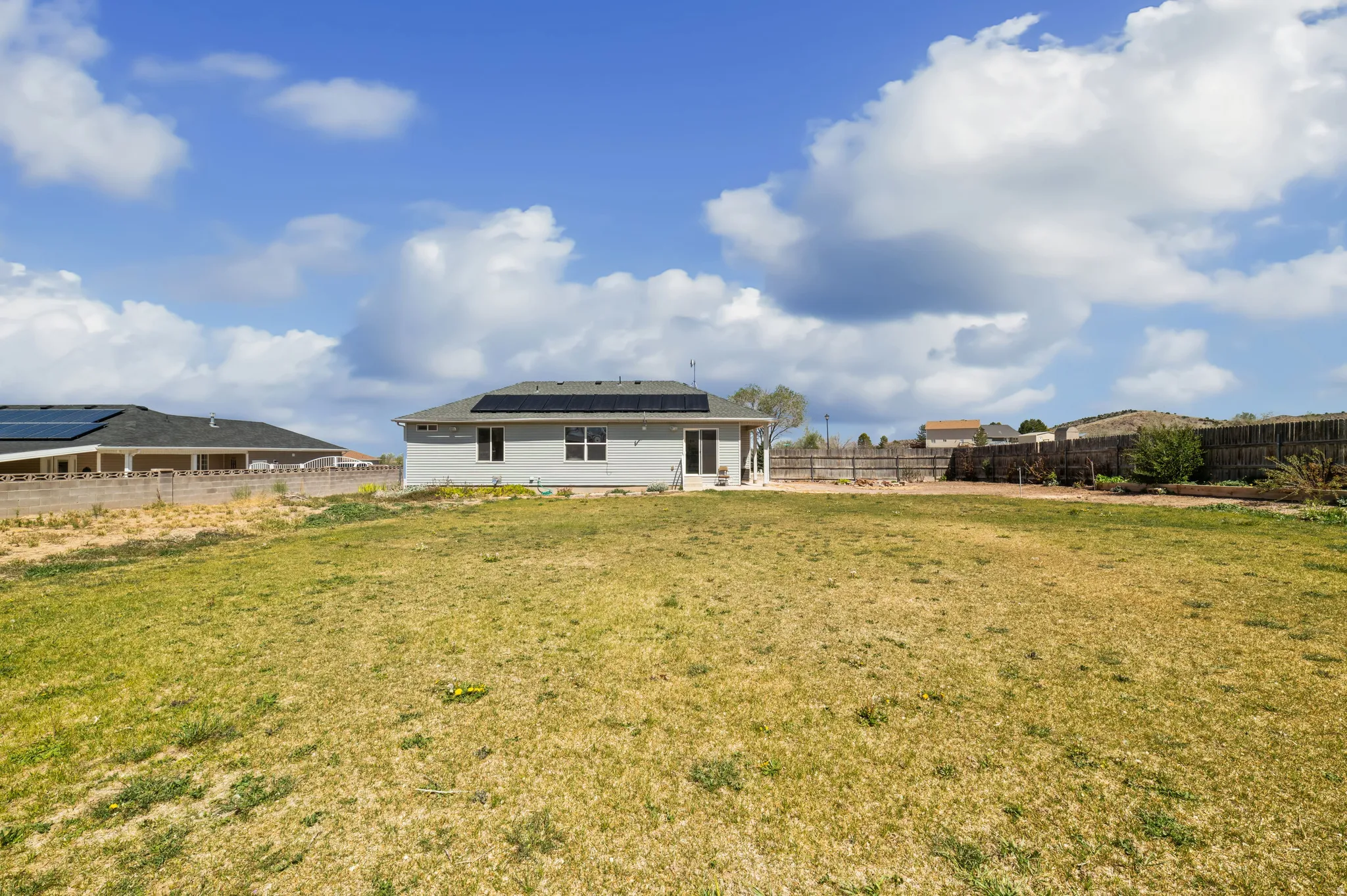 Back of house with roof mounted solar panels and a fenced backyard