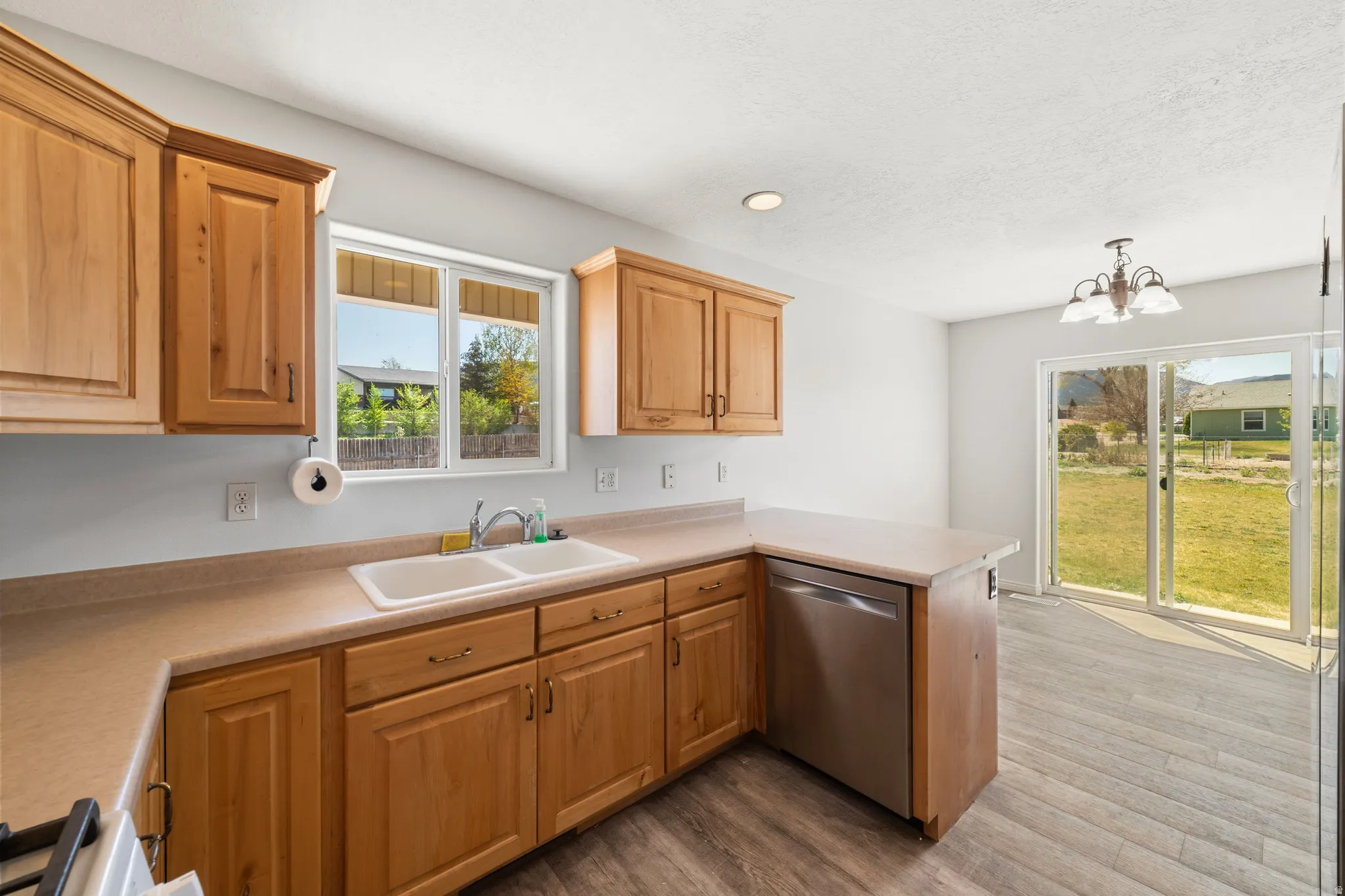 Kitchen featuring stainless steel dishwasher, a peninsula, light countertops, light wood-style flooring, and suspended lighting