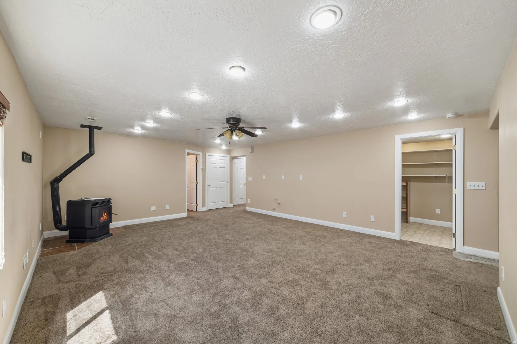 Below grade area with a wood stove, carpet, a textured ceiling, and ceiling fan