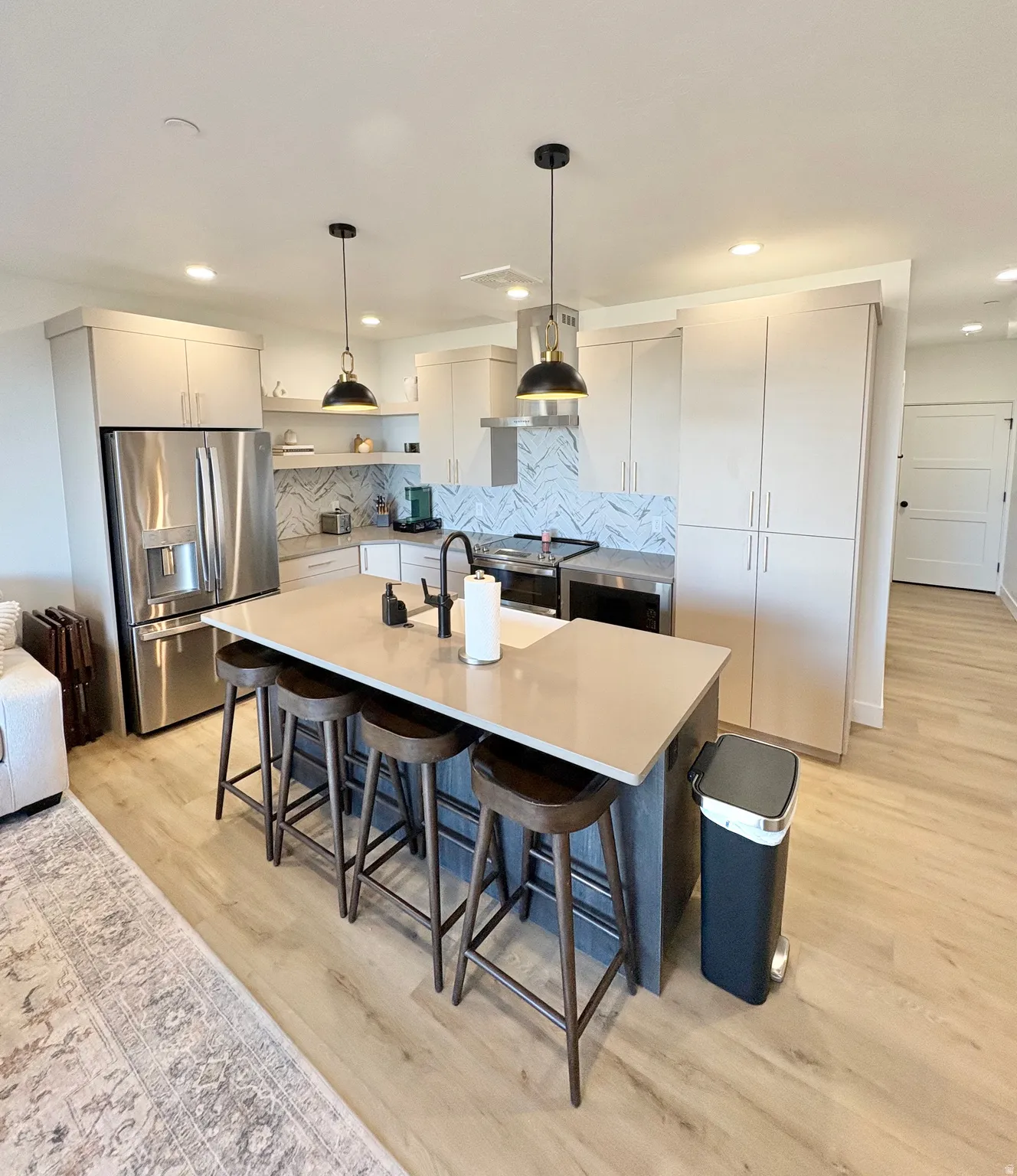 Kitchen featuring decorative light fixtures, stainless steel appliances, a kitchen bar, light wood finished floors, and an island with sink