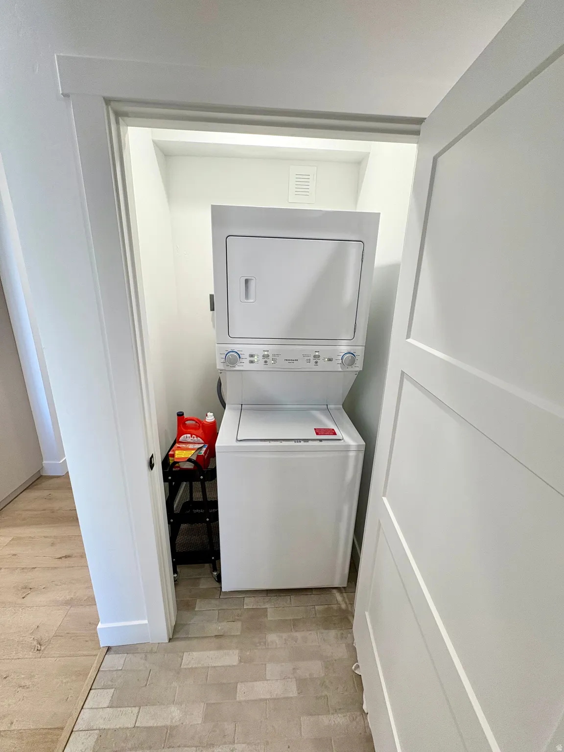 Laundry area with stacked washer and clothes dryer and light wood-style floors