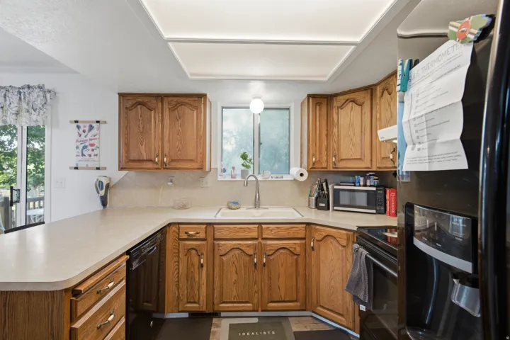 U-shaped kitchen with wood-finish cabinetry, solid surface countertops, a stainless steel sink, and a black dishwasher