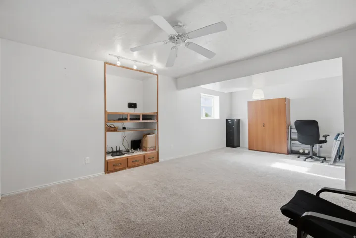 Built-in media center with wood-finish shelving and drawers, track lighting, ceiling fan, carpet flooring, and a window