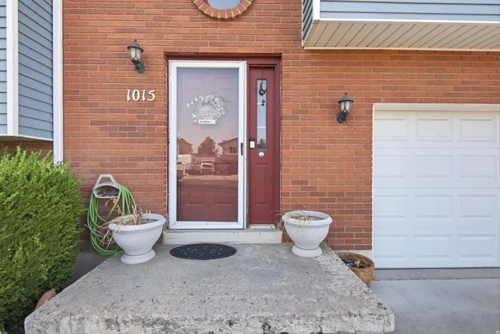 Brick facade with a red entry door, white garage door, and exterior sconce lighting