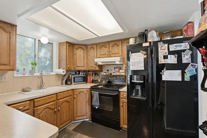 Wood-finish cabinetry, light-toned countertops, and a black appliance suite with a side-by-side refrigerator