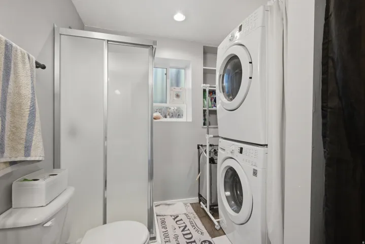 Shower enclosure with sliding frosted glass doors, a white toilet, and a stacked washer and dryer unit