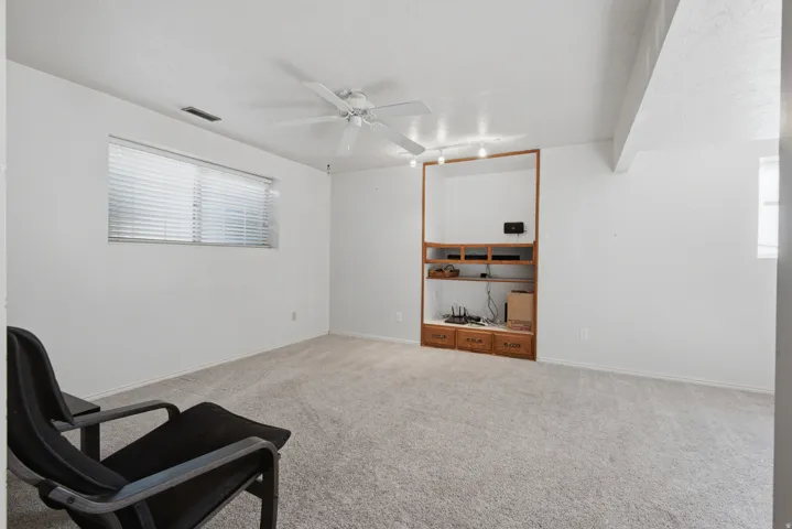 Carpeted room featuring a window with blinds, a ceiling fan, and built-in wood cabinetry with shelving