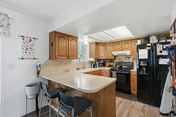 Kitchen featuring wood-finish cabinetry, a breakfast bar, recessed lighting, and black appliances including a refrigerator and range