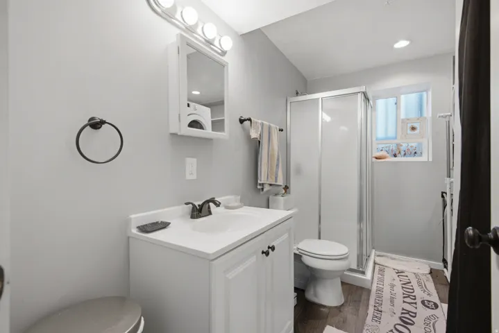 White vanity with an integrated sink, shower enclosure, and wood-finish flooring