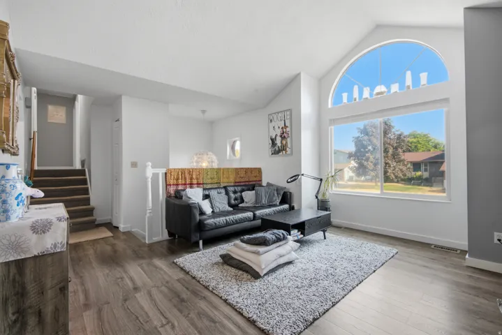Vaulted ceiling with an arched window, large rectangular window, wood-finish flooring, and a white baluster railing